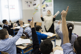 Classroom of Elementary school children seated at school desks raising hands