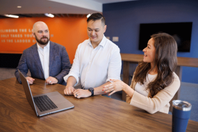 Three it managers stand in front of a laptop